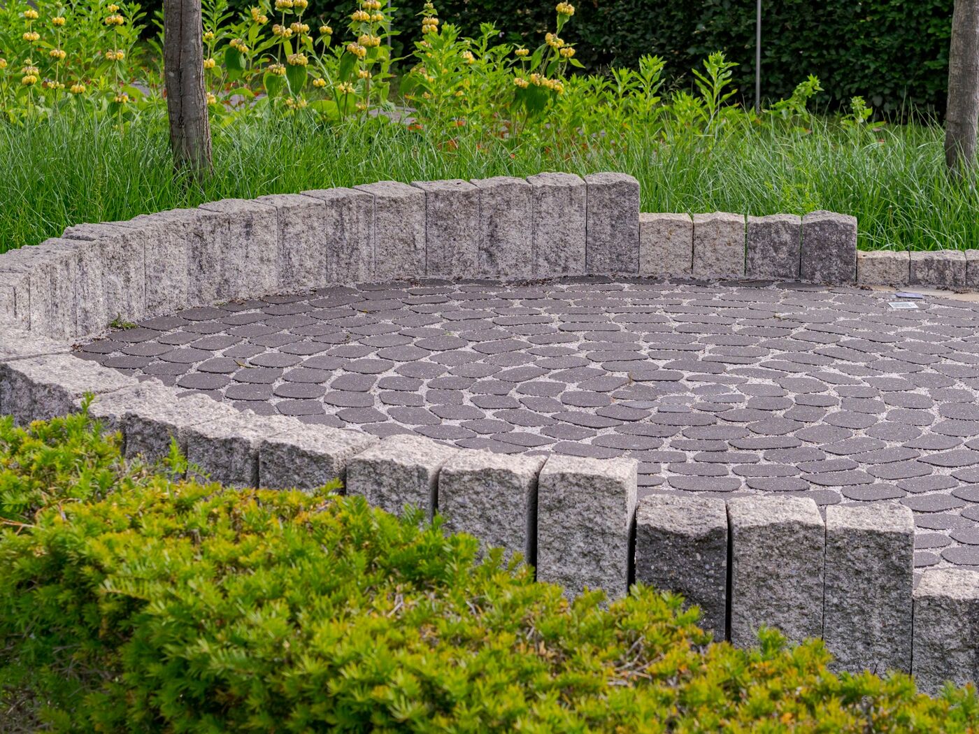 Kreisrund verlegte Pflasterfläche mit umlaufender Natursteinmauer und Bepflanzung